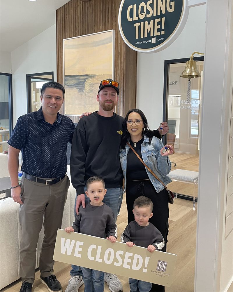 A family celebrating their home closing, holding their new keys and a We Closed sign